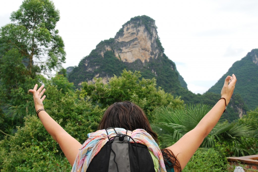 Mulher de mochila às costas virada para uma montanha verde
